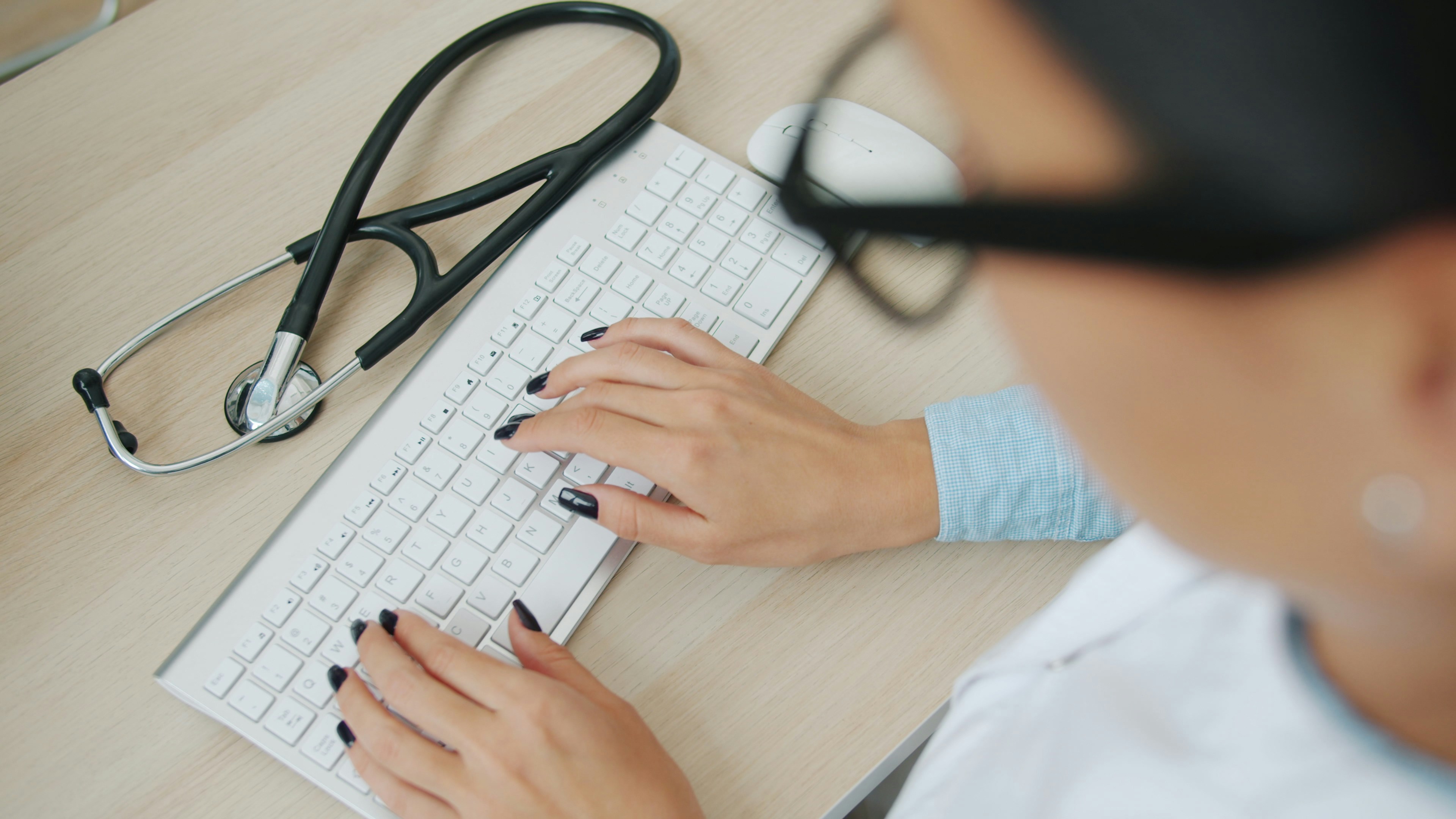 Image of female doctor typing on an apple keyboard with stethoscope by her