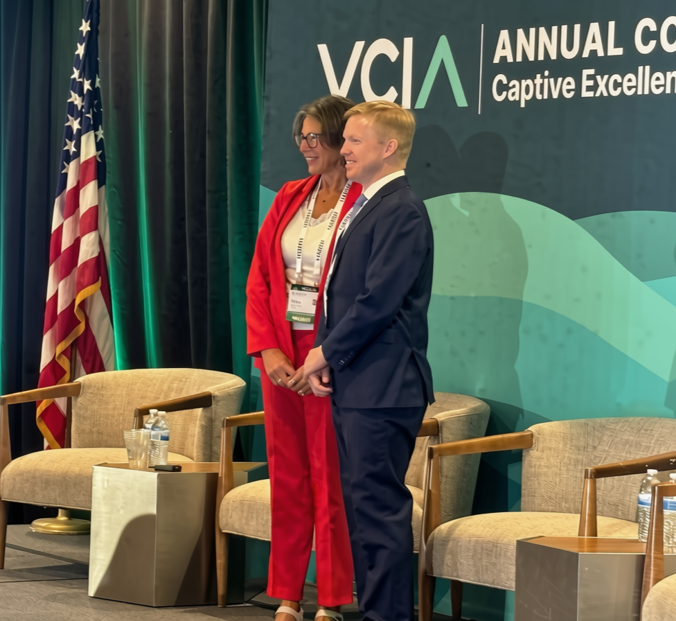 Tracy Hassett in red suit and VCIA President Ian Davis smiling after Tracy receives an award